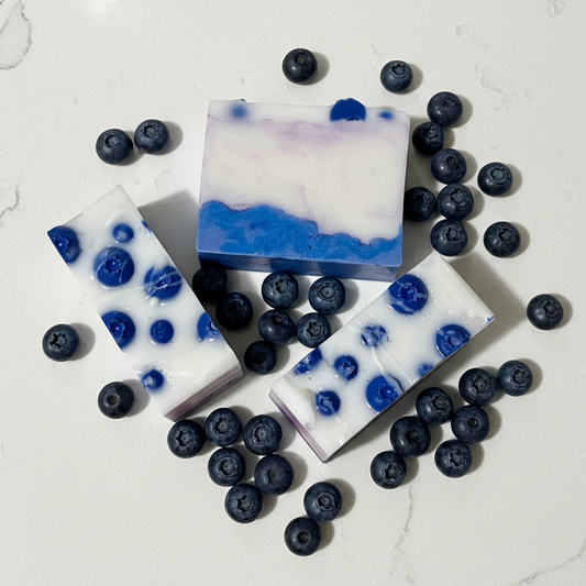 Three blueberry-themed soap bars on a white surface with scattered blueberries.
