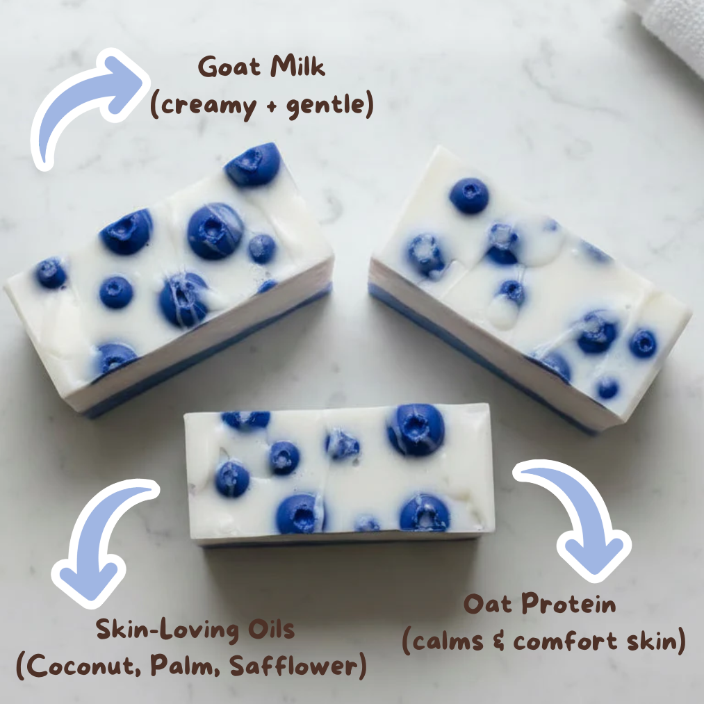 Goat milk soap bars with blueberries on a marble surface, labeled for ingredients.