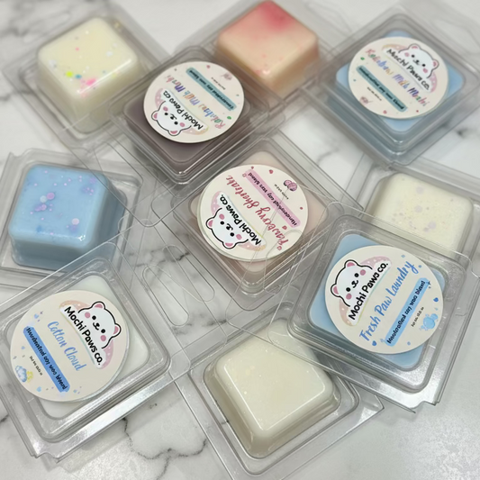 Collection of small wax melts in clear containers with visible labels on a marble surface.