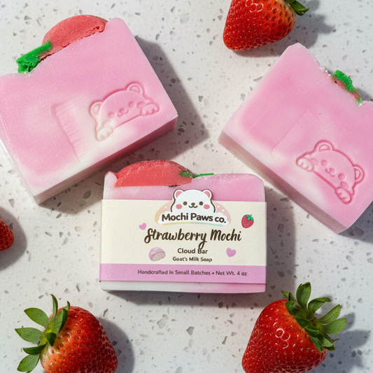 Pink strawberry soap bars with a bear design on a light surface surrounded by strawberries.